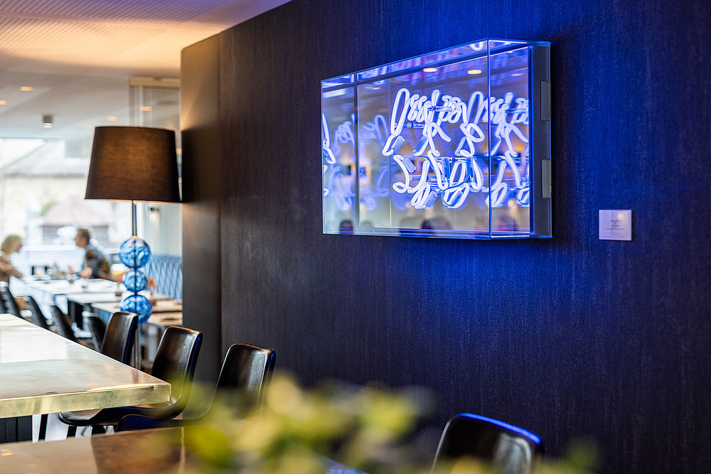 Glaskasten an der blauen Wand mit Neon-Lettern der Künstlerin Brigitte Kowanz im Restaurant des Hotel Stein in Salzburg