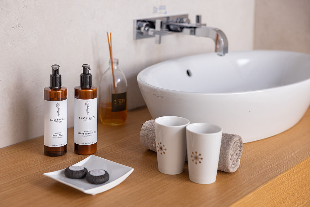 Badezimmer im Luxushotel Stein mit Naturkosmetik, Duftstäbchen und frisch aufgefrolltem Handtuch auf einer Waschkonsole