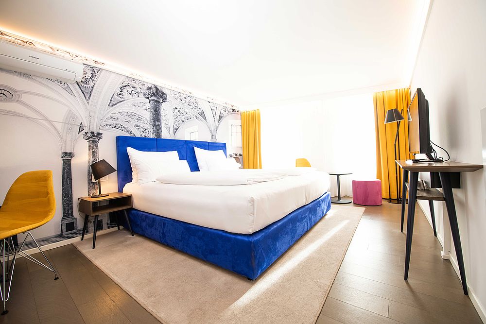 Doppelzimmer im Hotel Stein mit blauem Boxspringbett und einer Wandtapete mit römichen Säulen 