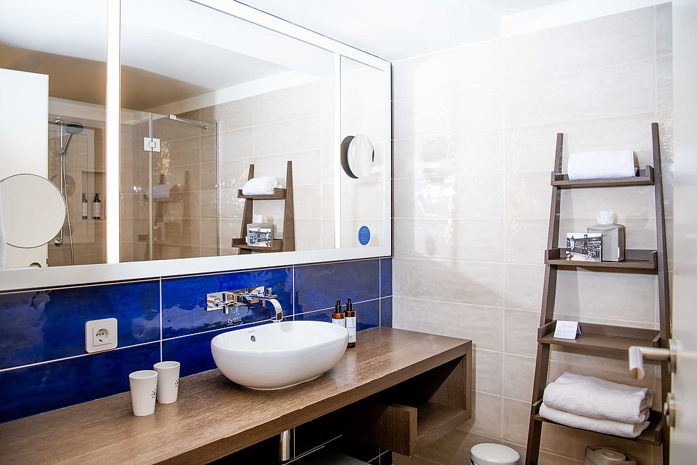 Badezimmer der Junior Suite im Hotel Stein mit blauen Fliesen, moderner Waschtischkonsole aus dunklem Holz und Glas-Duschkabine