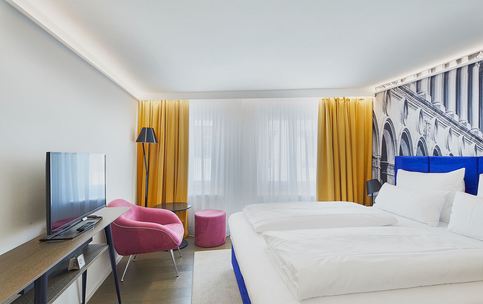 Ein modernes und helles Hotelzimmer mit großem Doppelbett, Fernseher, Sitzecke und moderner Wandtapete