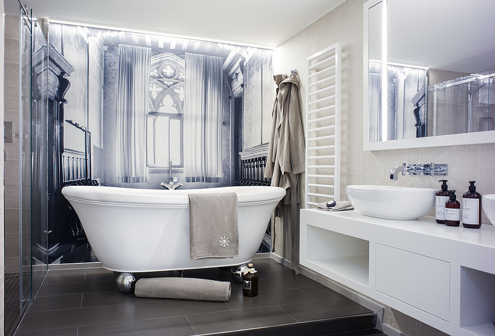 Modernes Badezimmer einer Suite mit freistehender Badewanne, schwarz-weißer Wandtapete und dunklem Fließen in Holzoptik