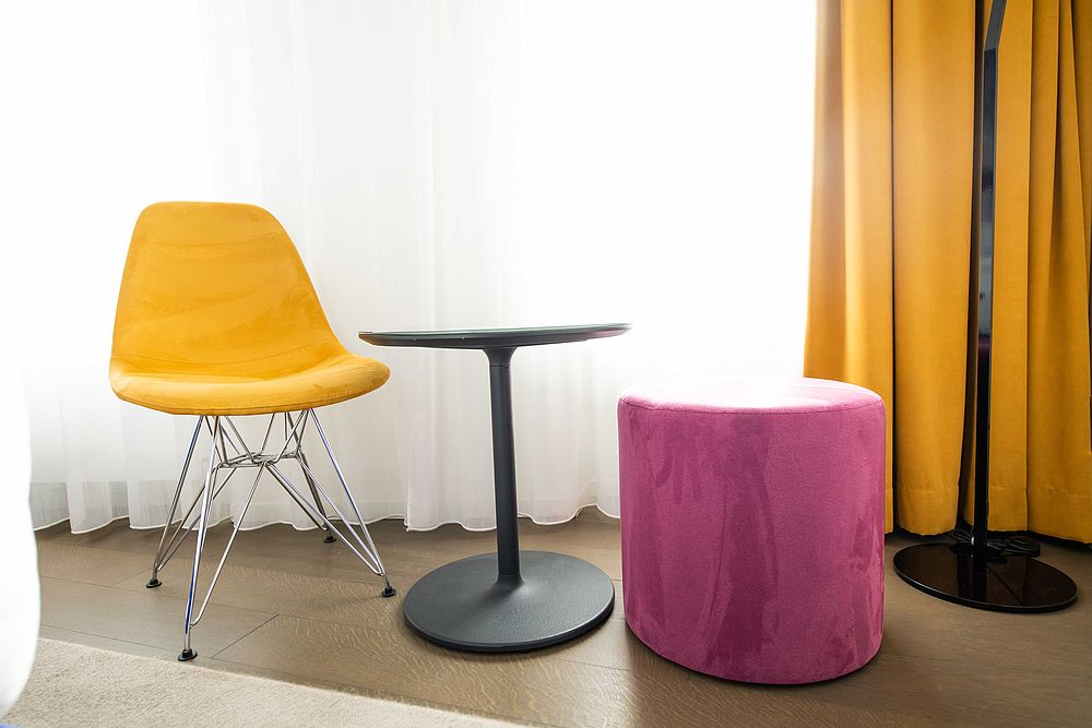 Gemütliche Sitzecke mit gelbem Designer-Sessel und pinken Hocker im Doppelzimmer des Hotel Stein