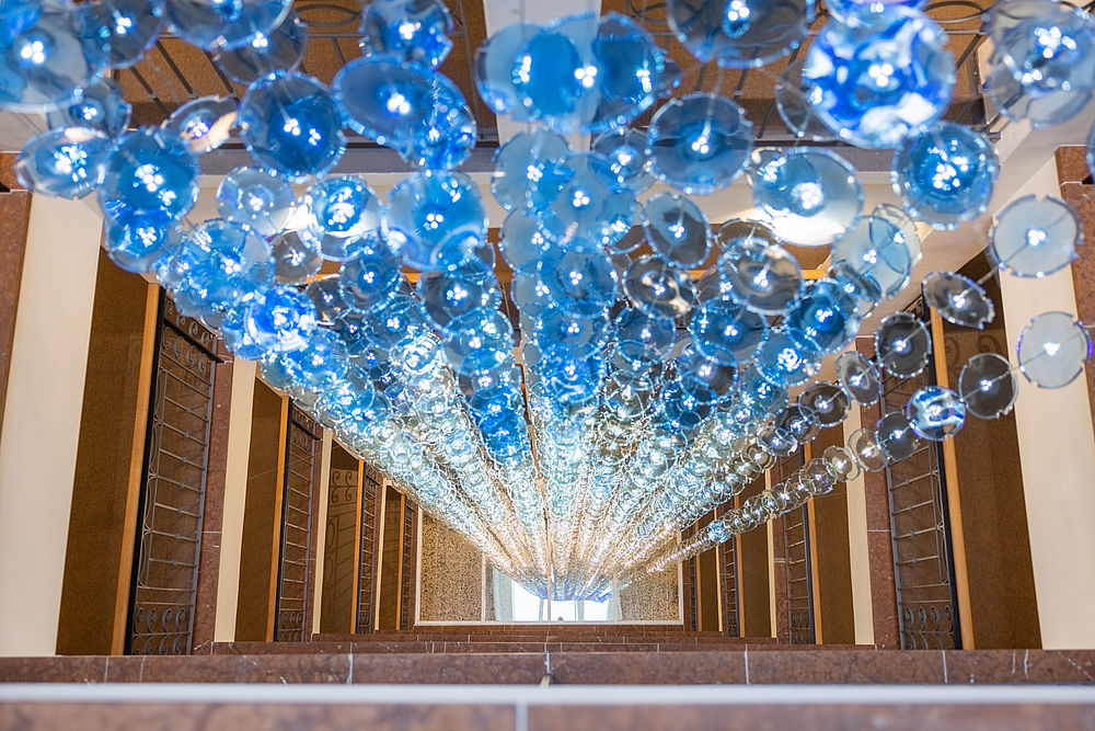 Hängende Kaskade aus hunderten Lichtern in blau-weißen Glasscheiben im Treppenhaus des Hotel Stein