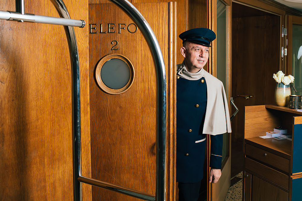 Ein Hotelmitarbeiter steht an einer historischen Holztür und trägt eine schicke Uniform mit Mütze