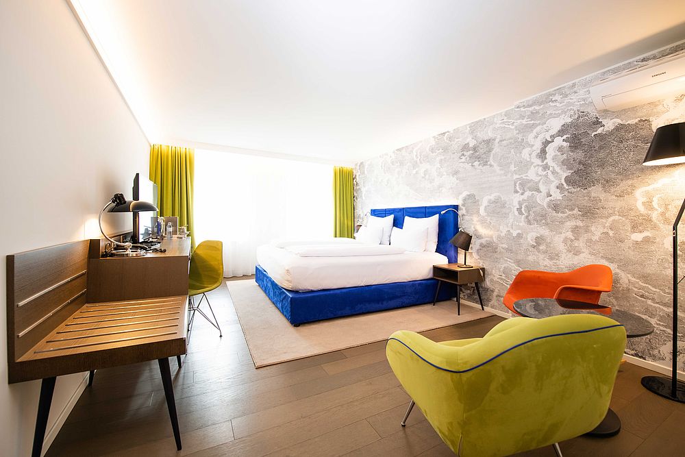 Junior Suite des Hotel Stein mit blauem Boxspringbett vor schwarz-weiß Wolken-Tapete und Sitzecke mit bunten Polstermöbel
