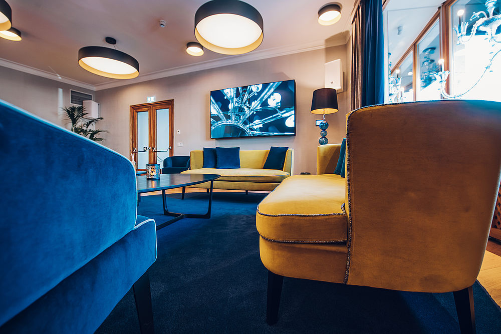 Lounge des Hotels mit großen blauen und gelben Sesseln aus Samt und großen, runden Deckenlampen
