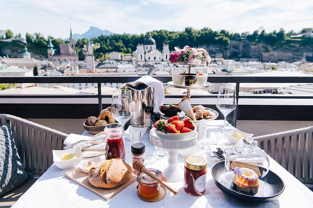 Ein reich gedeckter Frühstückstisch auf der Dachterrasse des Hotel Stein mit Blick auf Salzburgs Sehenswürdigkeiten