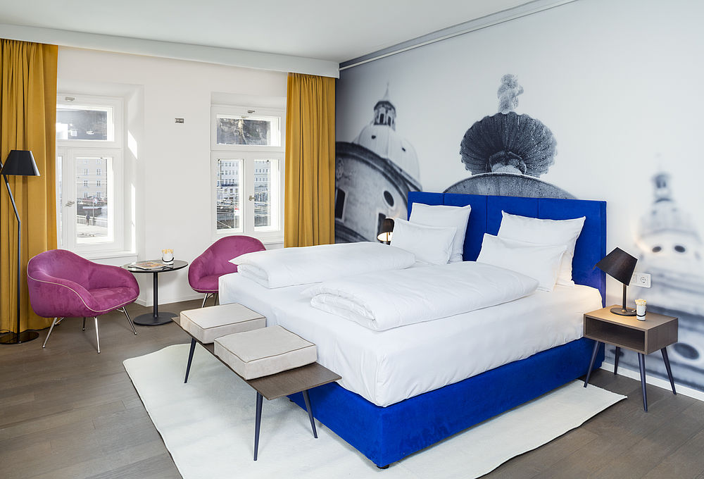 Junior suite in the design hotel Stein with a comfortable box-spring bed and a seating area by the window with a view of Salzburg city centre