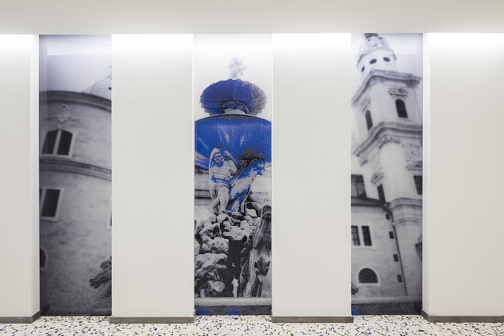 Der Hotelflur mit großen Aufnahmen des Salzburger Residenzplatzes mit Brunnen und blauen Akzenten