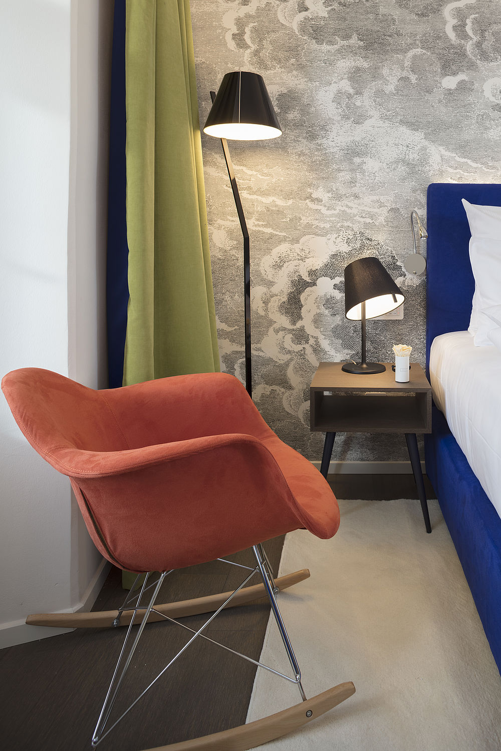 Design-Schaukelstuhl in orange neben dem Bett eines Hotelzimmers