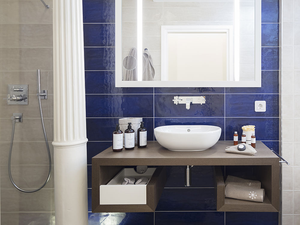 Waschbecken eines Hotelzimmers mit Spiegel, blauen Fließen und Pflegeprodukten