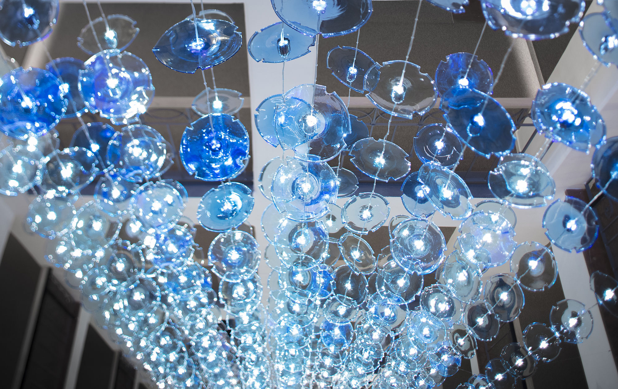 Glaskunst aus blauen Glasplatten, die an Schnüren angebracht sind und das Licht spiegeln