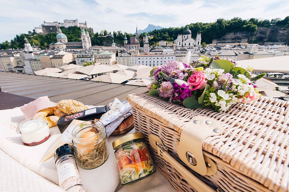 Picknickkorb kunstvoll drapiert mit Blumen und Frühstück auf einer weißen Decke der Dachterrasse des Hotel Stein