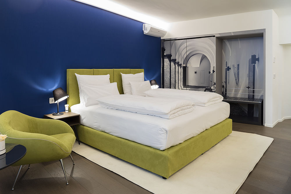 Das Schlafzimmer der Junior Suite des Hotels mit königsblauer Tapete und grünem Bett und Sessel