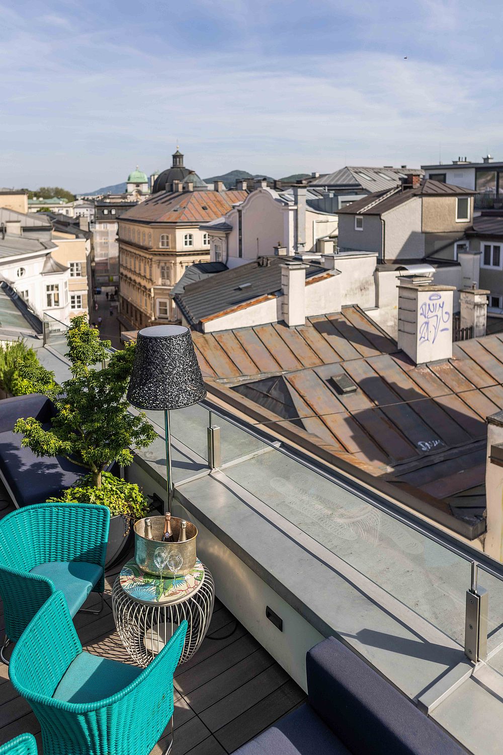 Terrasse des Hotel Stein mit blauen Rattan-Sesseln, Champagnerflaschen in einer Silberschale auf einem Metalltisch und Blick über die Dächer von Salzburg