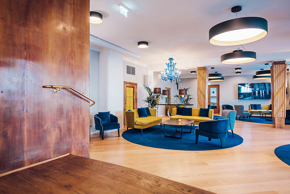 Der Loungebereich mit blauen und gelben Sesseln aus Samt, sowie braunen Säulen aus Holz