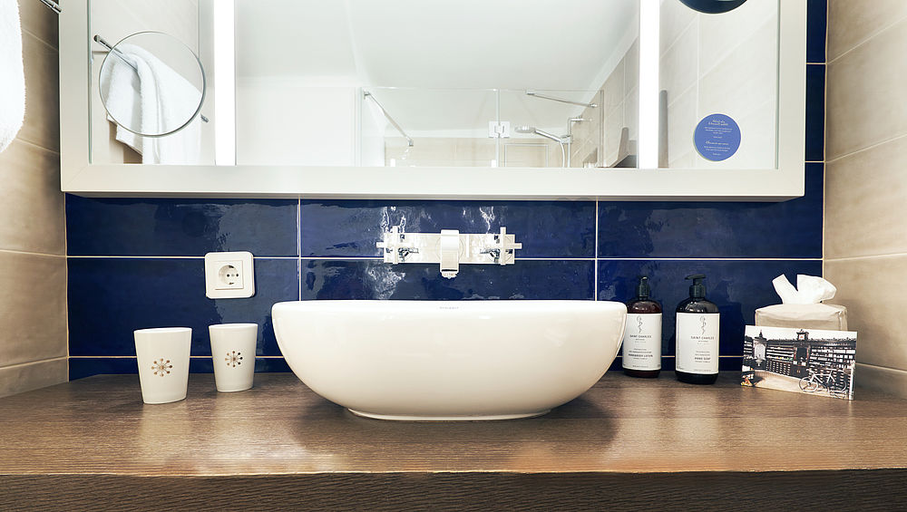 Der Waschtisch eines Badezimmers ist ausgestattet mit einem Waschbecken, großem Spiegel und Pflegeprodukten