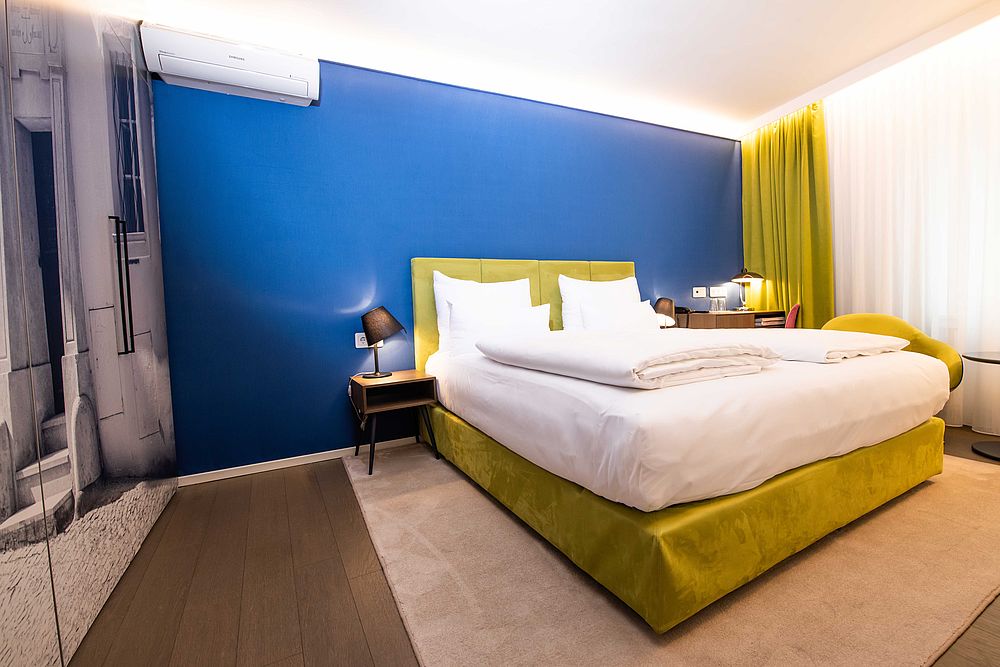 Doppelzimmer im Hotel Stein mit blauem Boxspringbett und einer Wandtapete mit römischen Säulen 